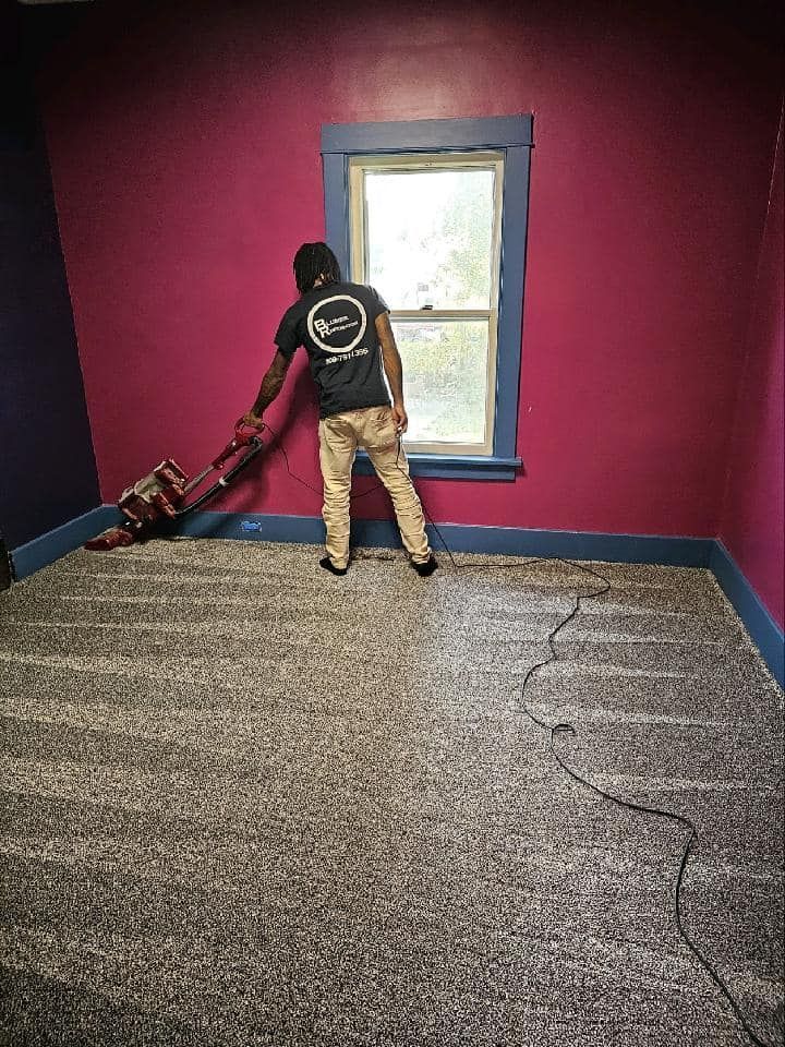 A man is vacuuming the floor of a room with pink walls.