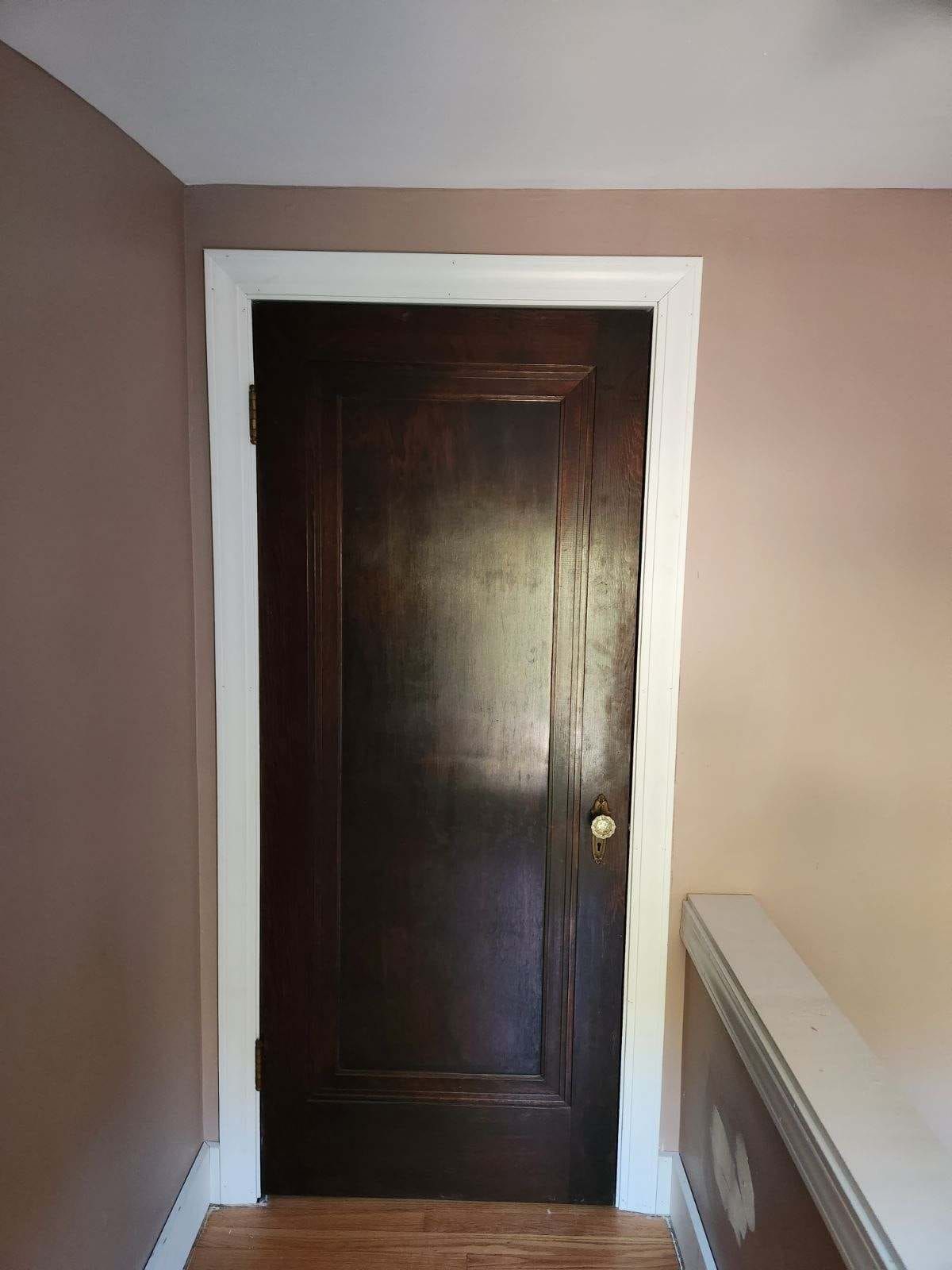 A brown door with a white trim is in a room with pink walls.