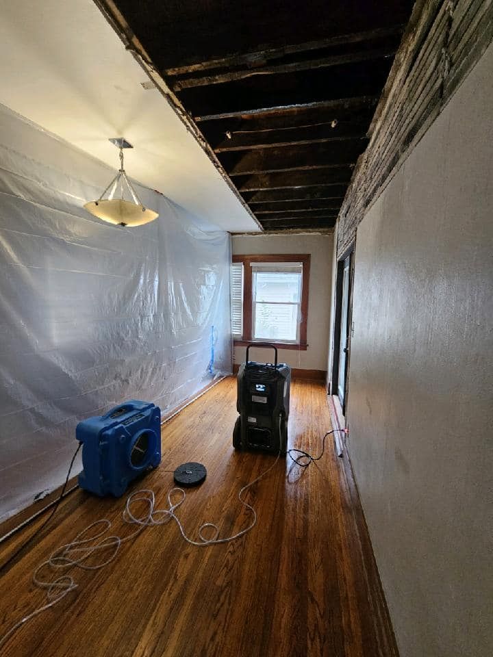 A hallway with wooden floors and a plastic sheet on the wall.