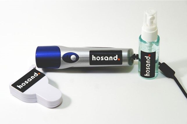 Torcia elettrica Hosand argento e blu con disinfettante ed etichetta, su superficie bianca.