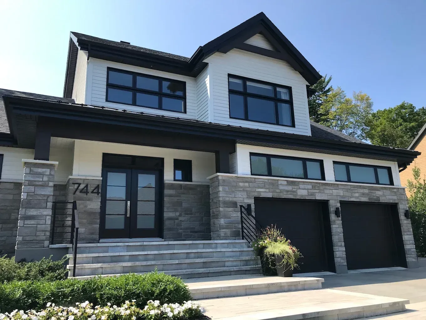 Peinture résidentielle extérieure sur grande maison blanche avec toit noir et deux garages