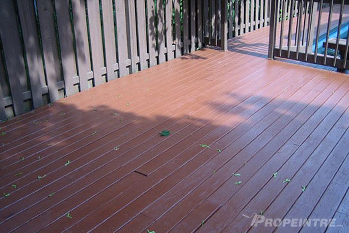 Teinture de patio en bois réalisée par Propeintre, avec clôture et piscine en arrière-plan