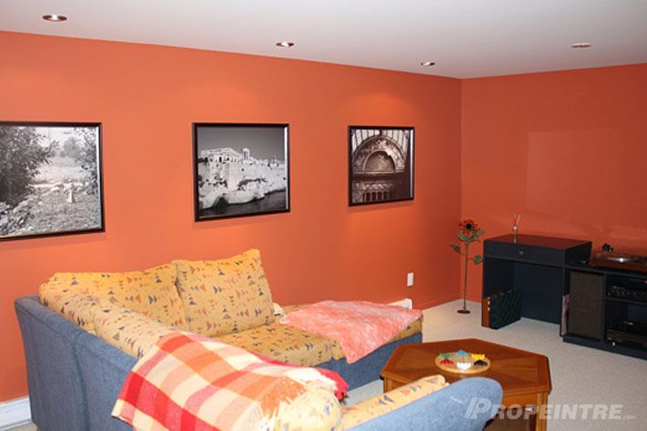 Un salon avec des murs orange et un canapé, peinture intérieure professionnelle réalisée par Propeintre
