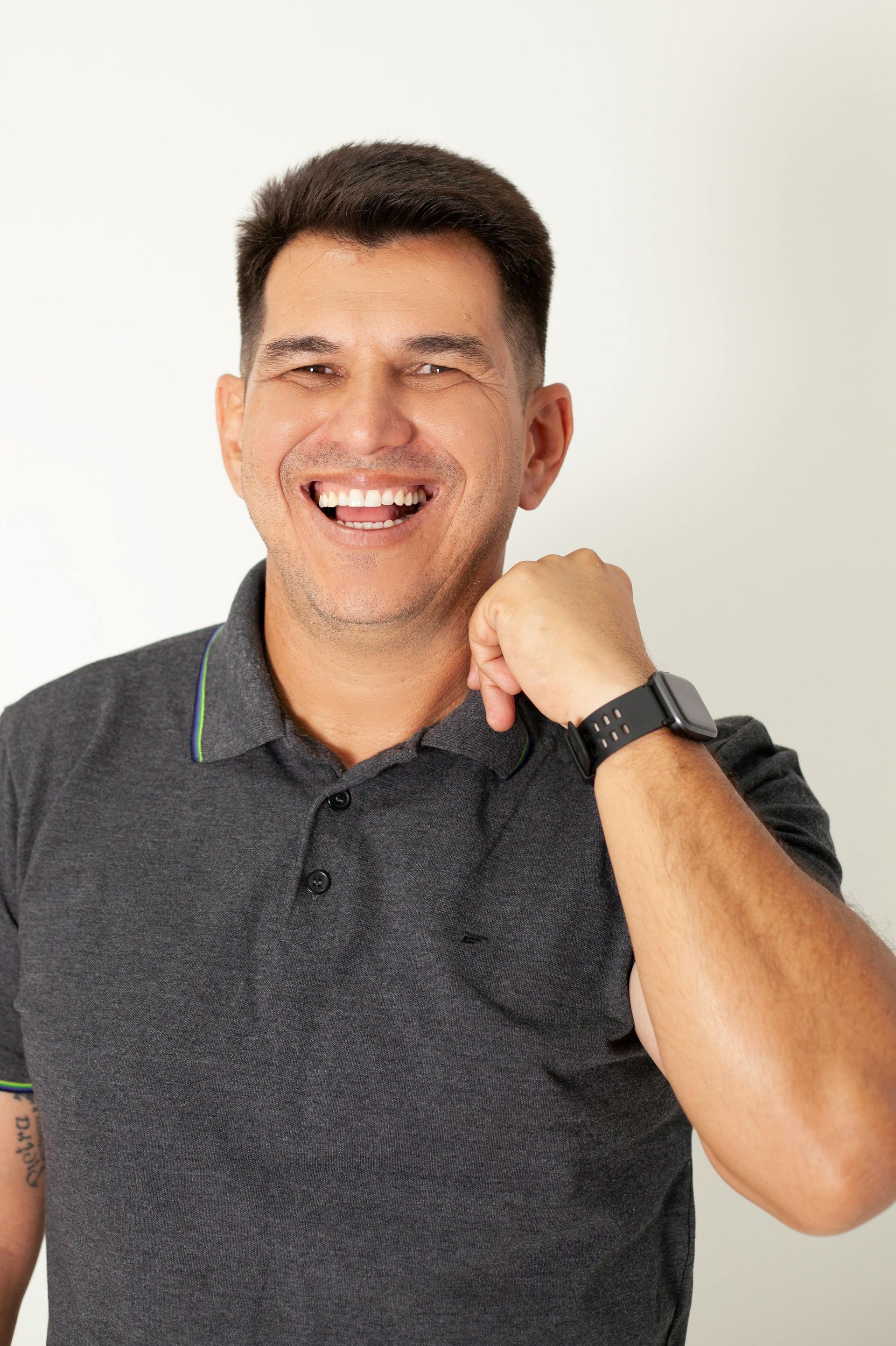 Smiling person in a dark polo shirt with a black watch, raising a fist against a light background