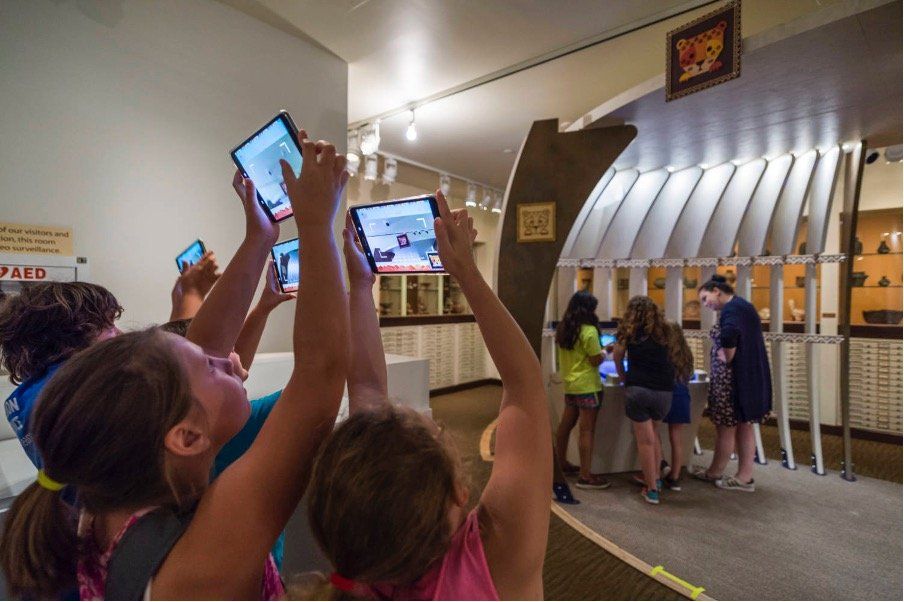 A group of children are playing with their phones in a museum.