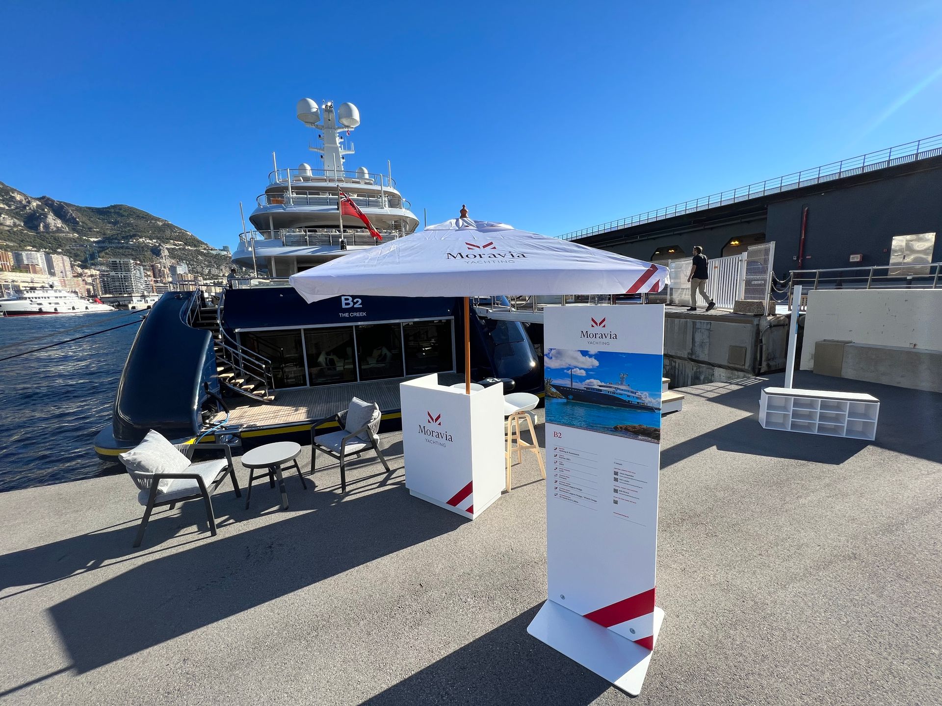A large yacht is docked in a harbor next to a table and umbrella.