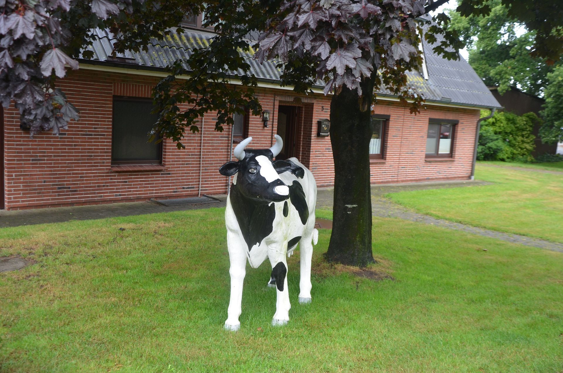 Eine schwarz-weiße Kuhstatue vor einem Backsteingebäude und einem Baum.