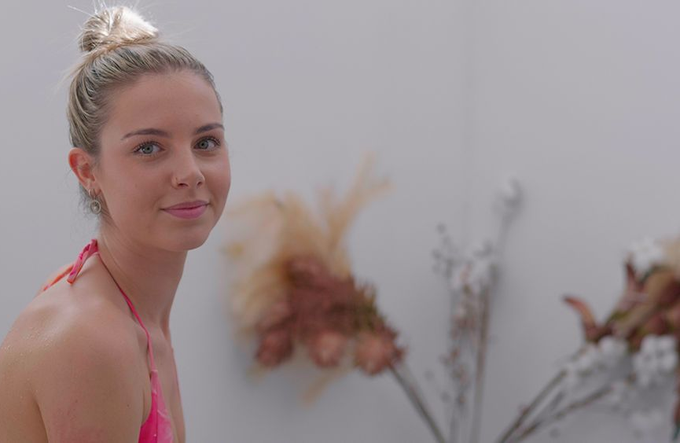 A woman in a pink bikini is standing next to a vase of flowers — Figtree Day Spa in Sawtell, NSW