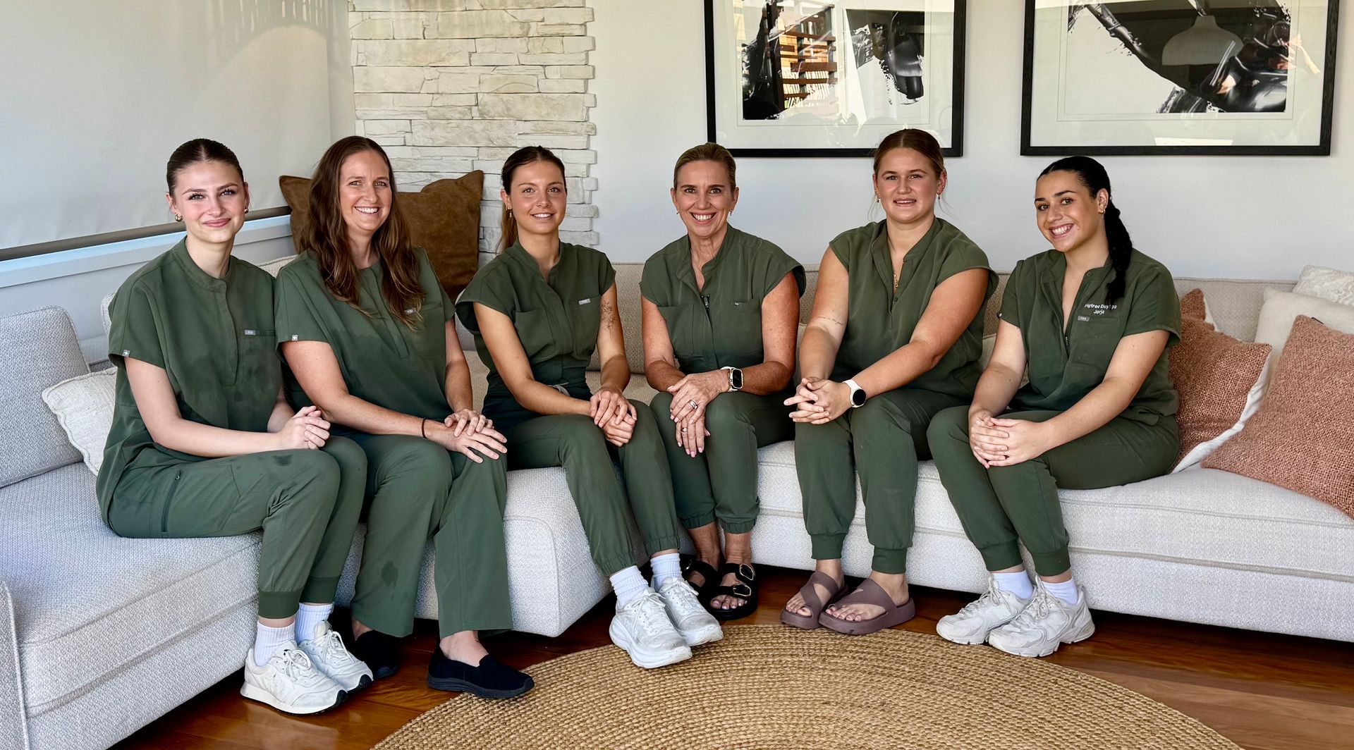 Six females wearing green uniform sitting on sofa — Figtree Day Spa in Sawtell, NSW