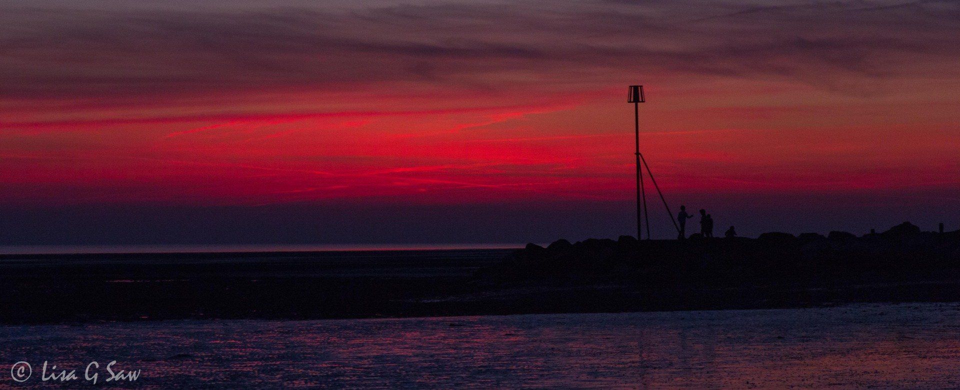 Children playing on groin at beach at dusk, red sky