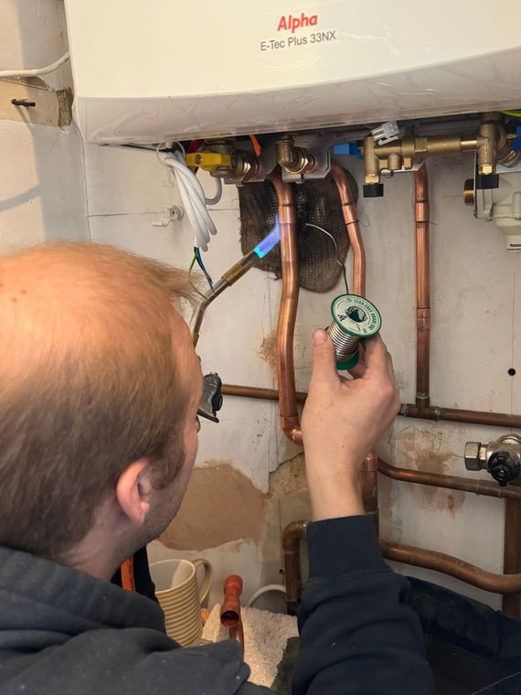 Plumber using a torch to work on copper pipes connected to a boiler.