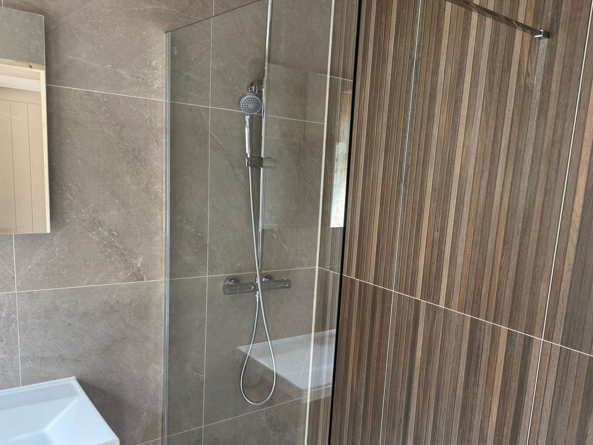 Shower stall with glass door, silver fixtures, and brown-toned tile walls.