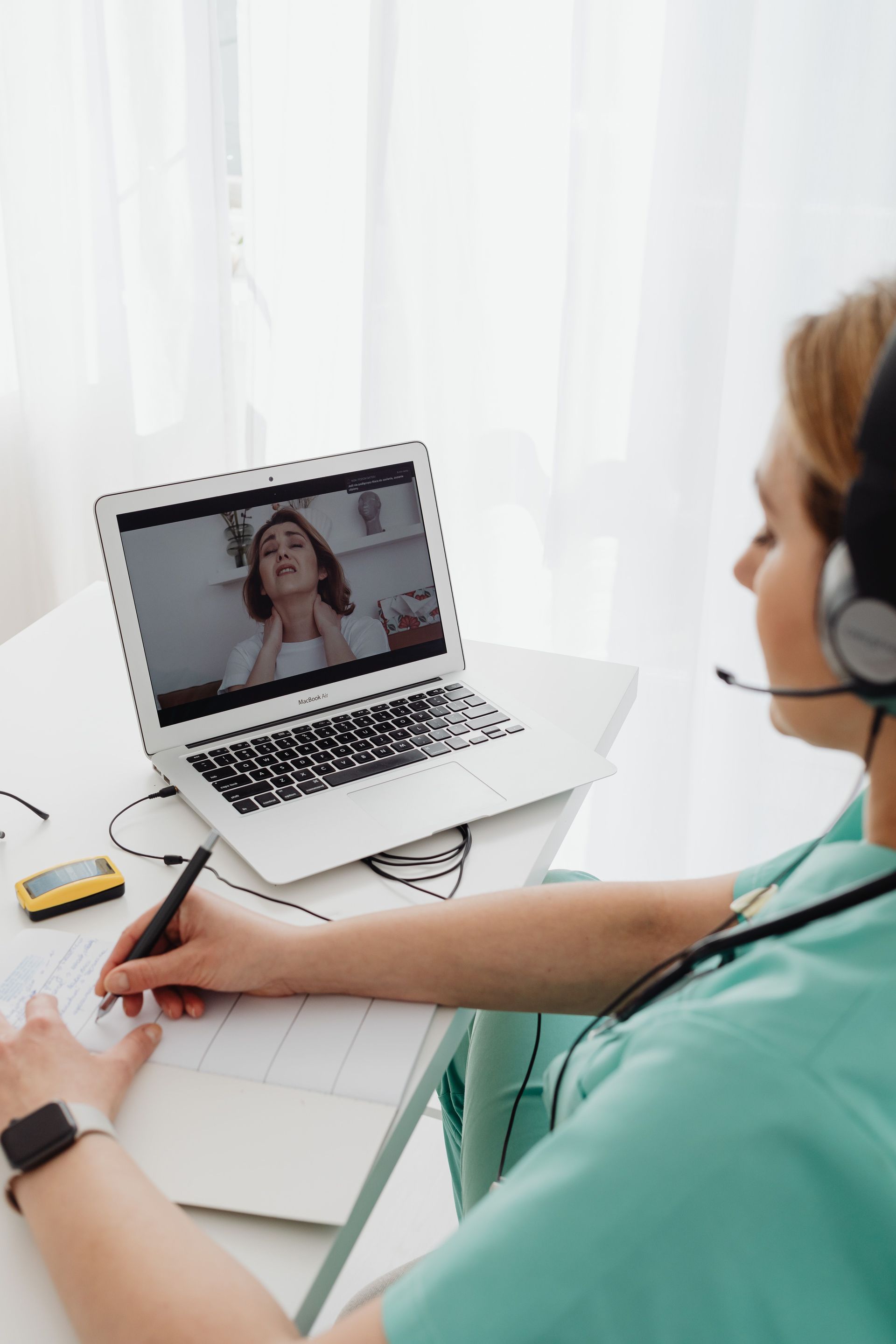 Person taking notes during a laptop video call in a bright office