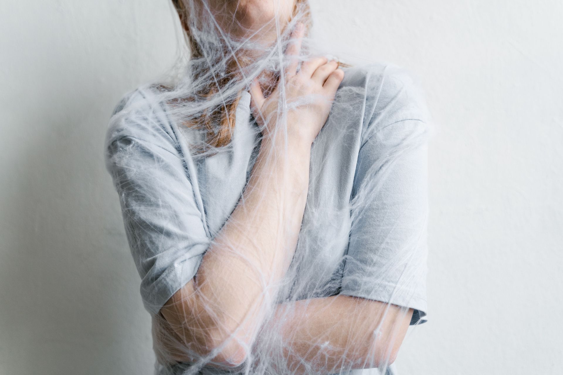 Person in a gray shirt with a translucent veil, standing against a light background.