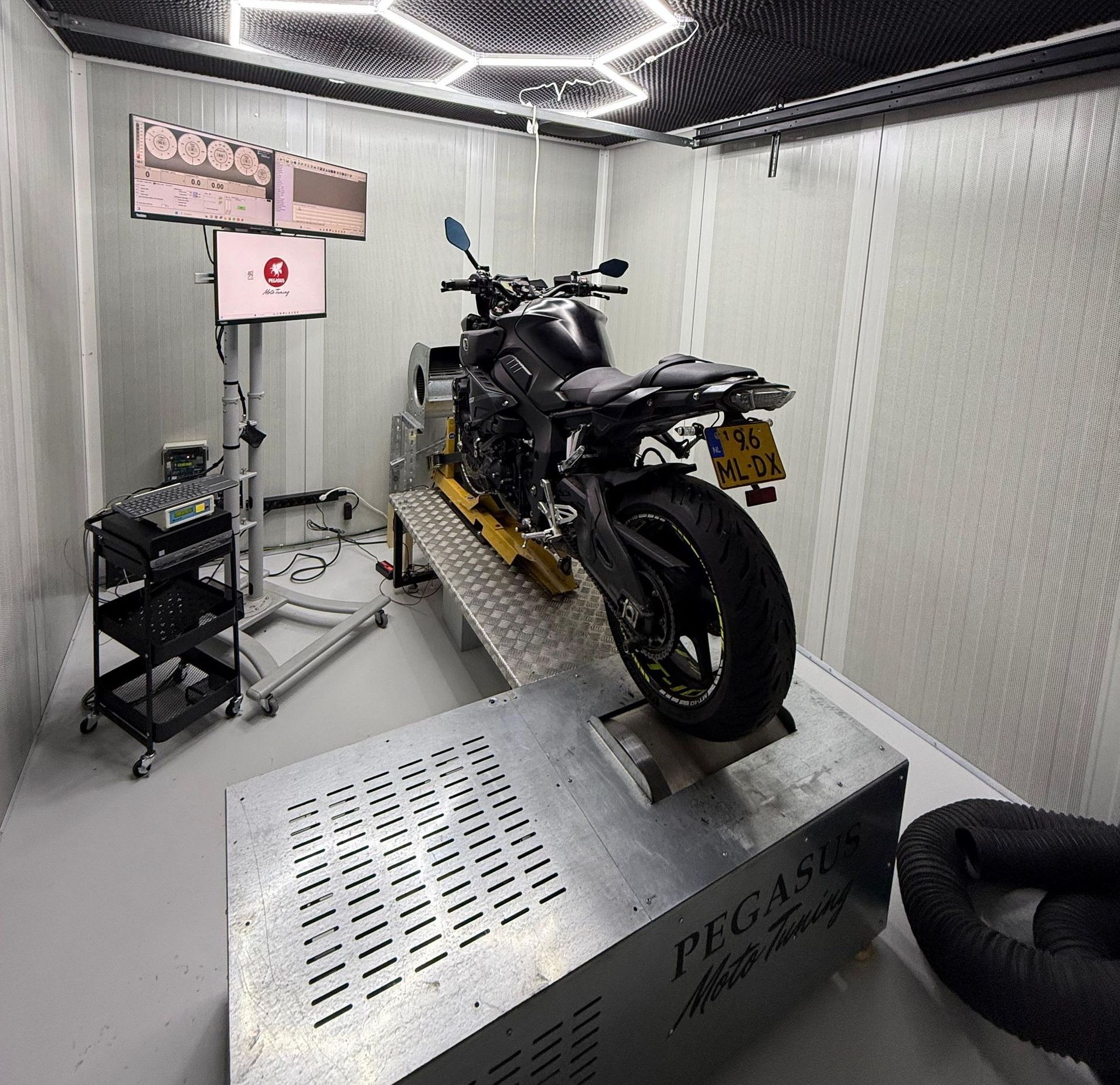 Een motorfiets op een dynamometer in een testruimte, met apparatuur en beeldschermen.