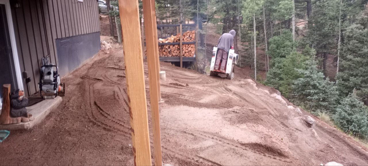 A man is driving a bulldozer on a dirt road next to a house.
