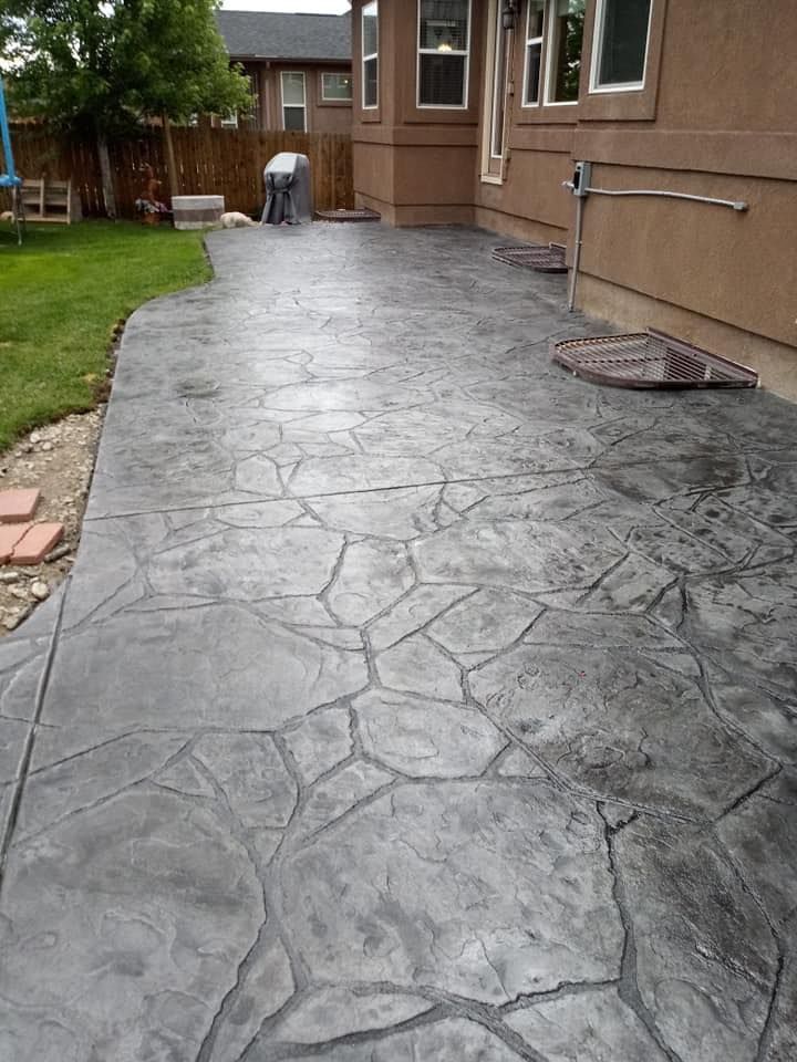 Stamped concrete patio beside a house with a wet, gray stone pattern and lawn nearby