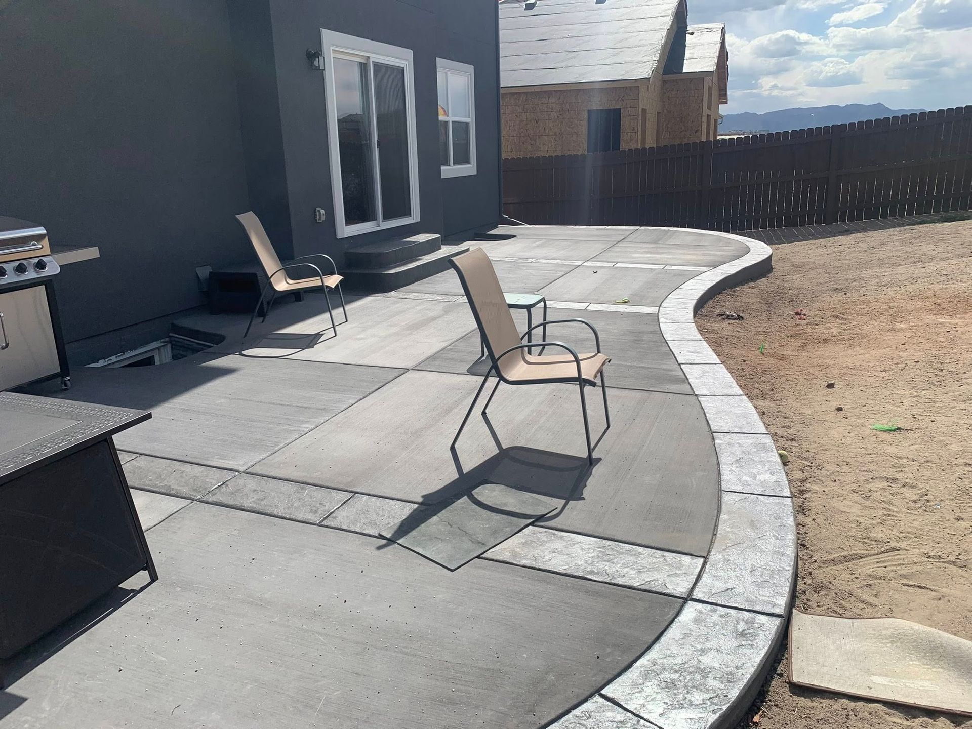 Patio with curved concrete walkway, two chairs, and a dark house exterior beside a gravel yard