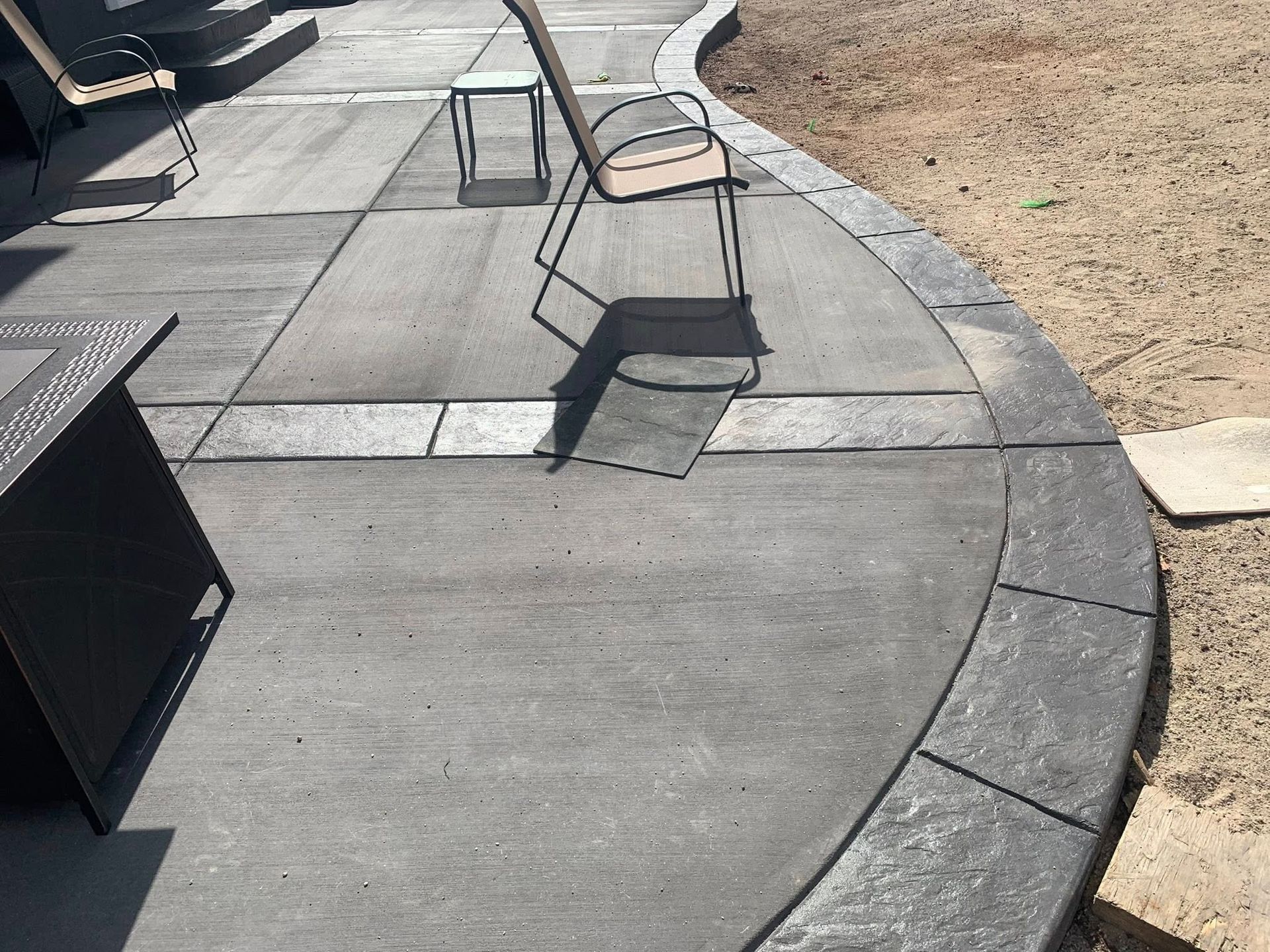 Curved concrete patio with metal chairs beside a sandy area in bright sunlight