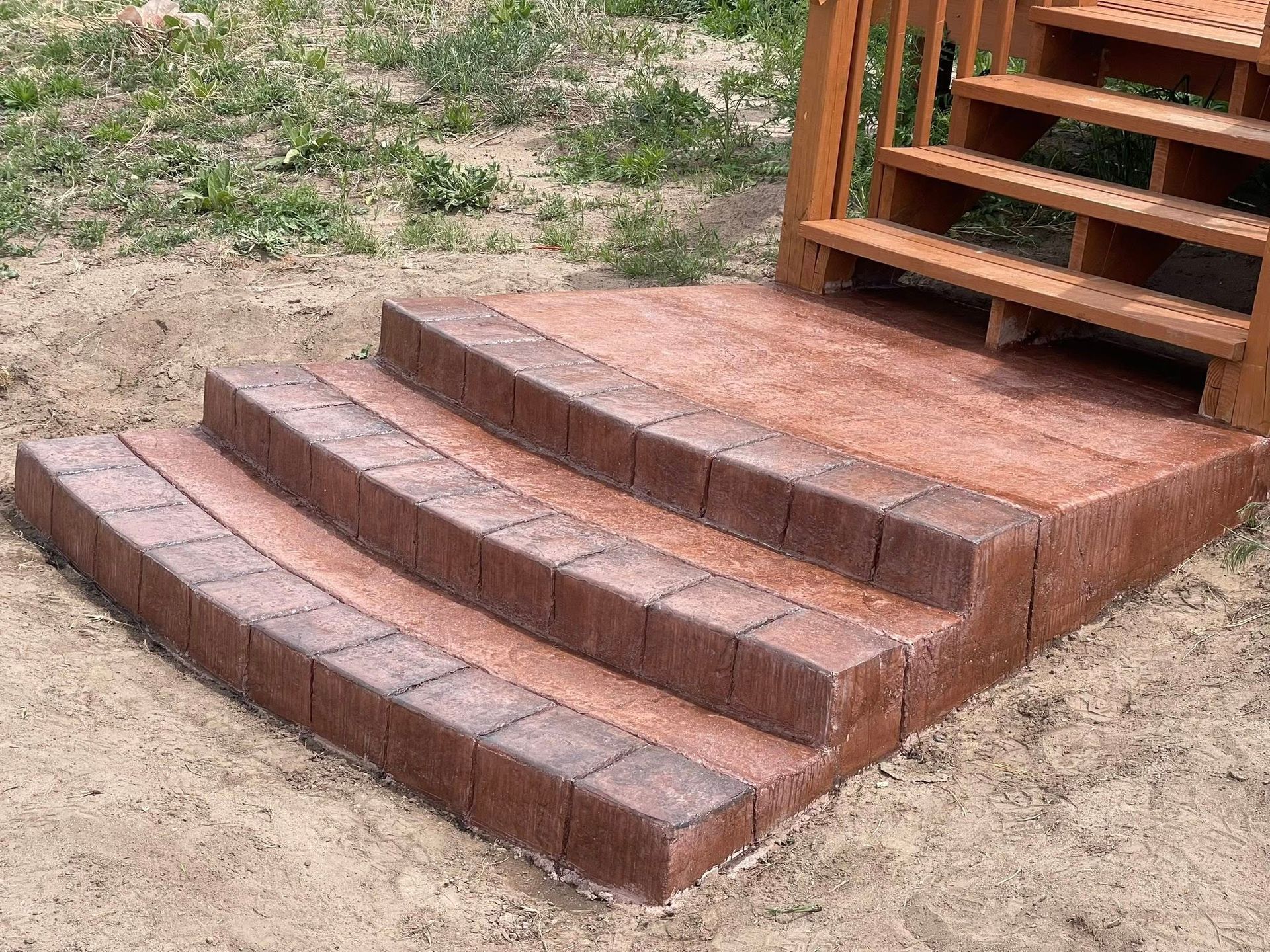 Brick steps leading up to a wooden deck on a dirt yard