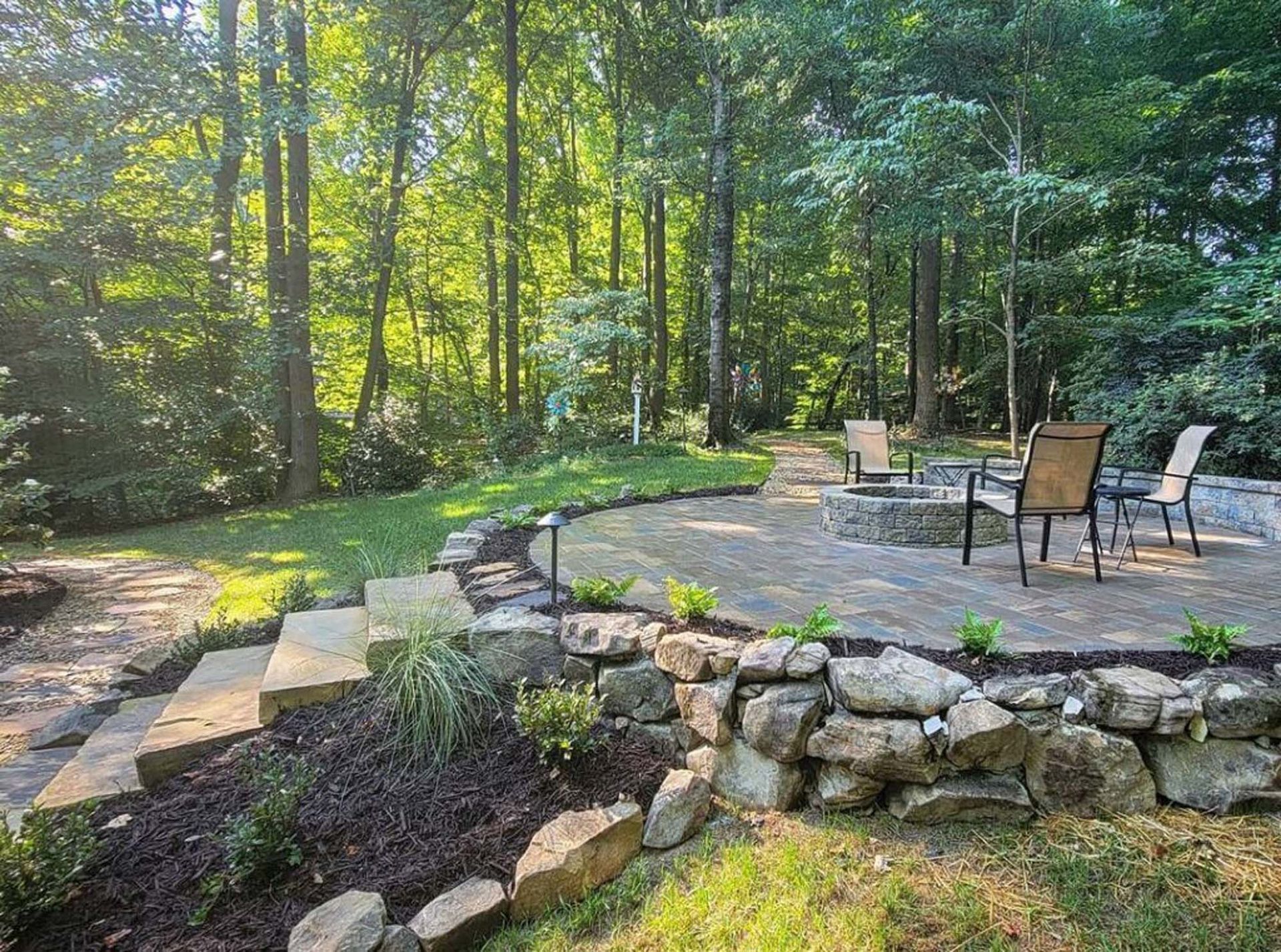 A patio with chairs and a fire pit in the middle of a forest.