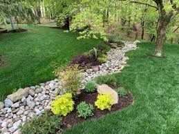 A stream running through a lush green yard surrounded by trees and rocks.