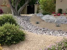 A garden with rocks , bushes and flowers in front of a house.
