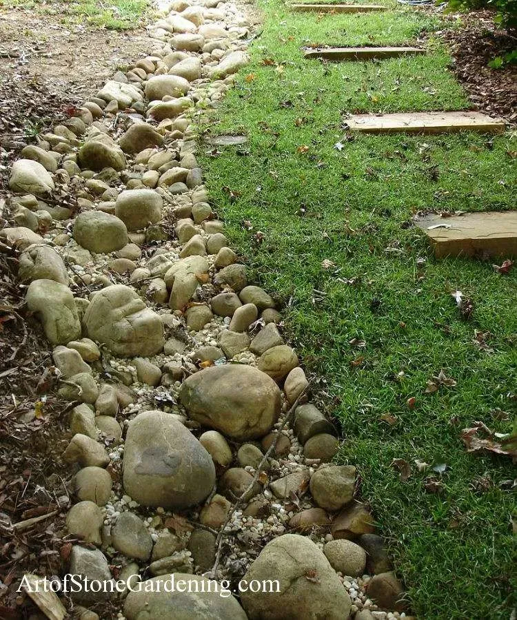 A path made of rocks is going through a lush green field.