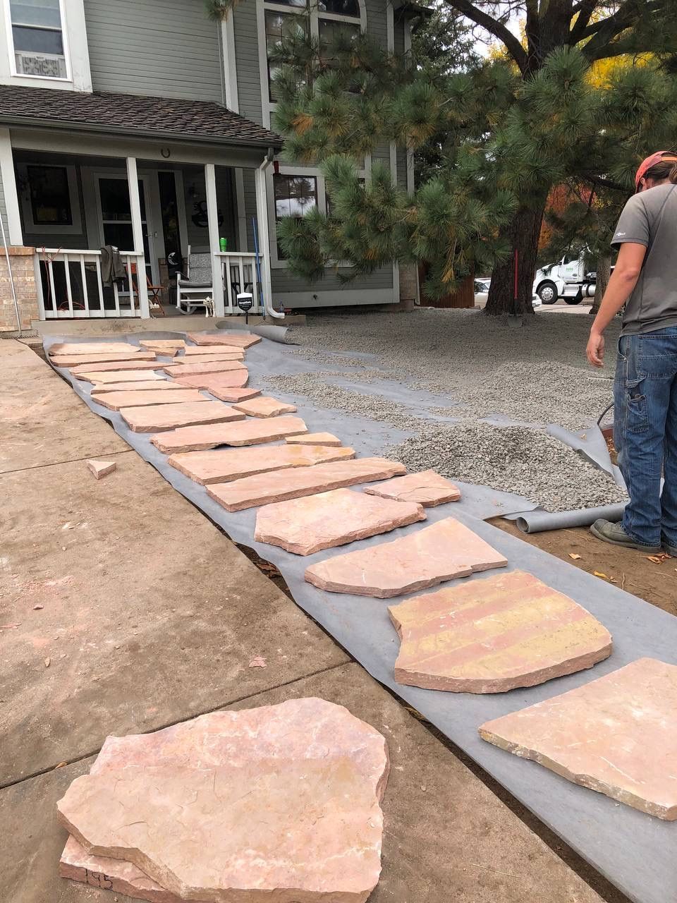 Stone walkway under construction leading to a porch, with a worker on the right and gravel along the path.