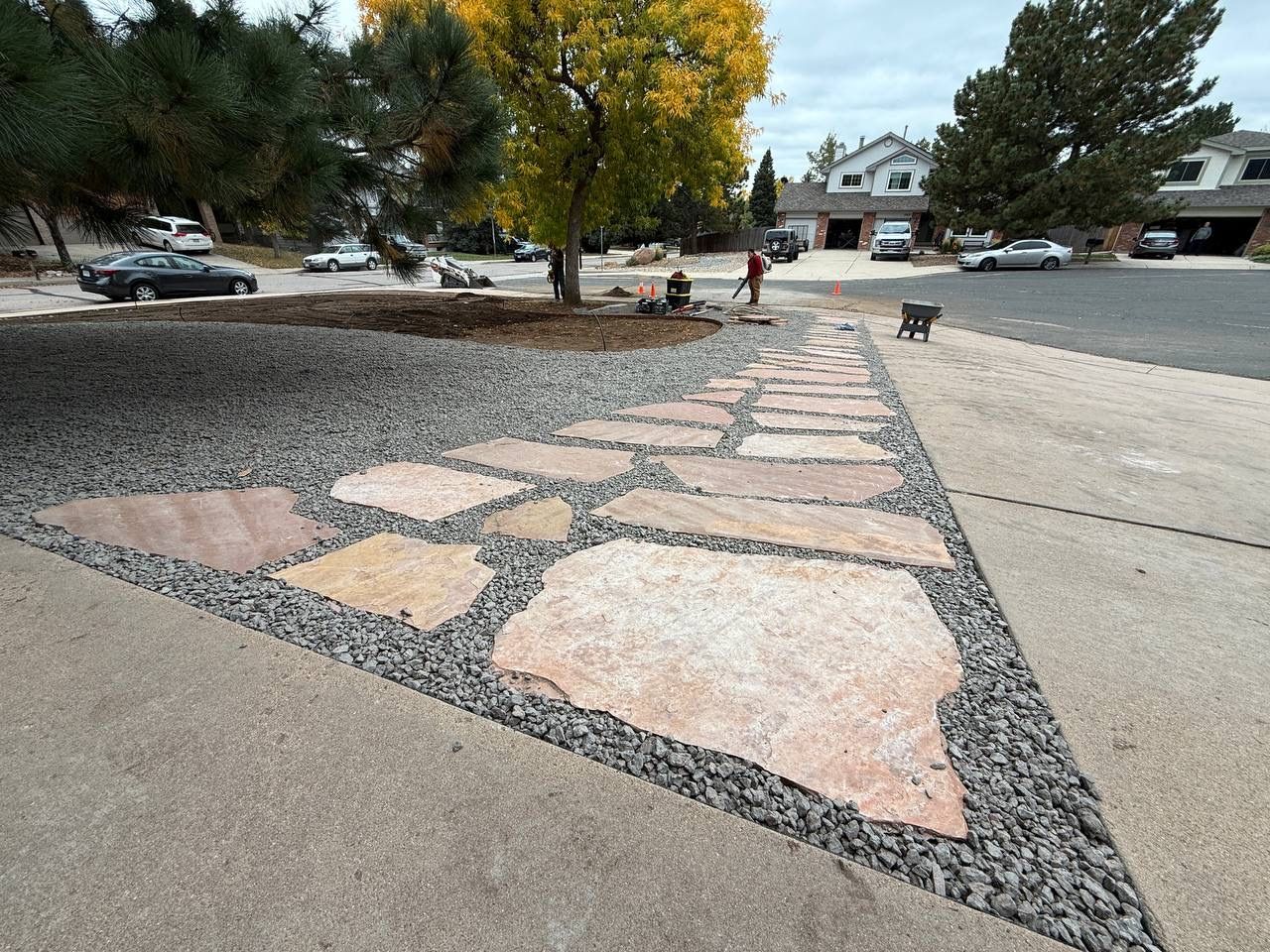 Stone mosaic path in a parking lot with trees and a few people in the distance.