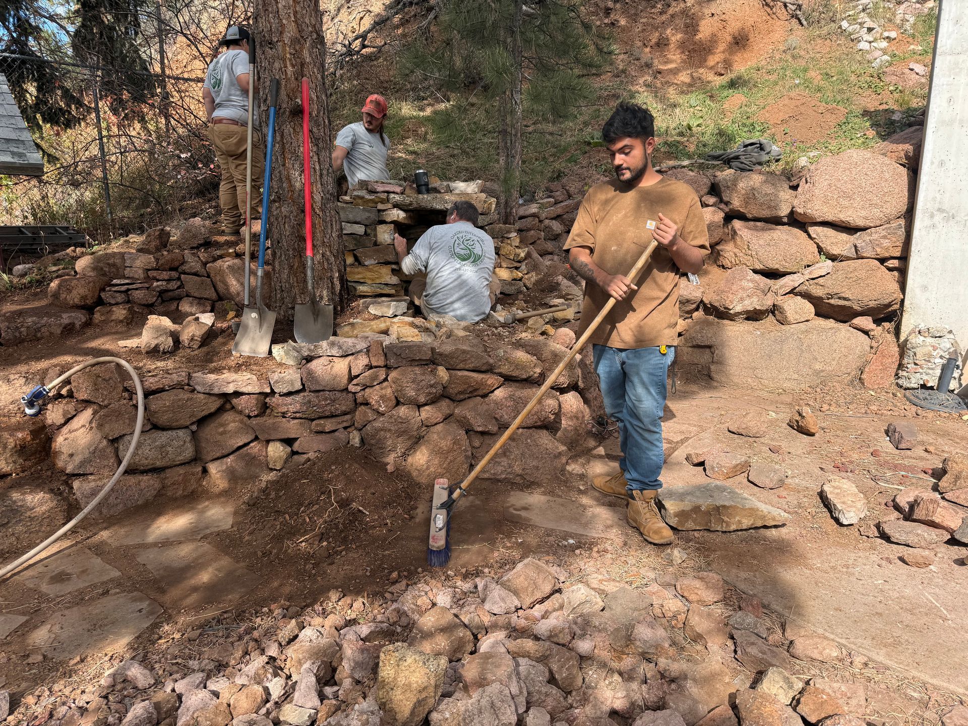 Workers repairing a stone wall and digging earth with tools on a rocky hillside.