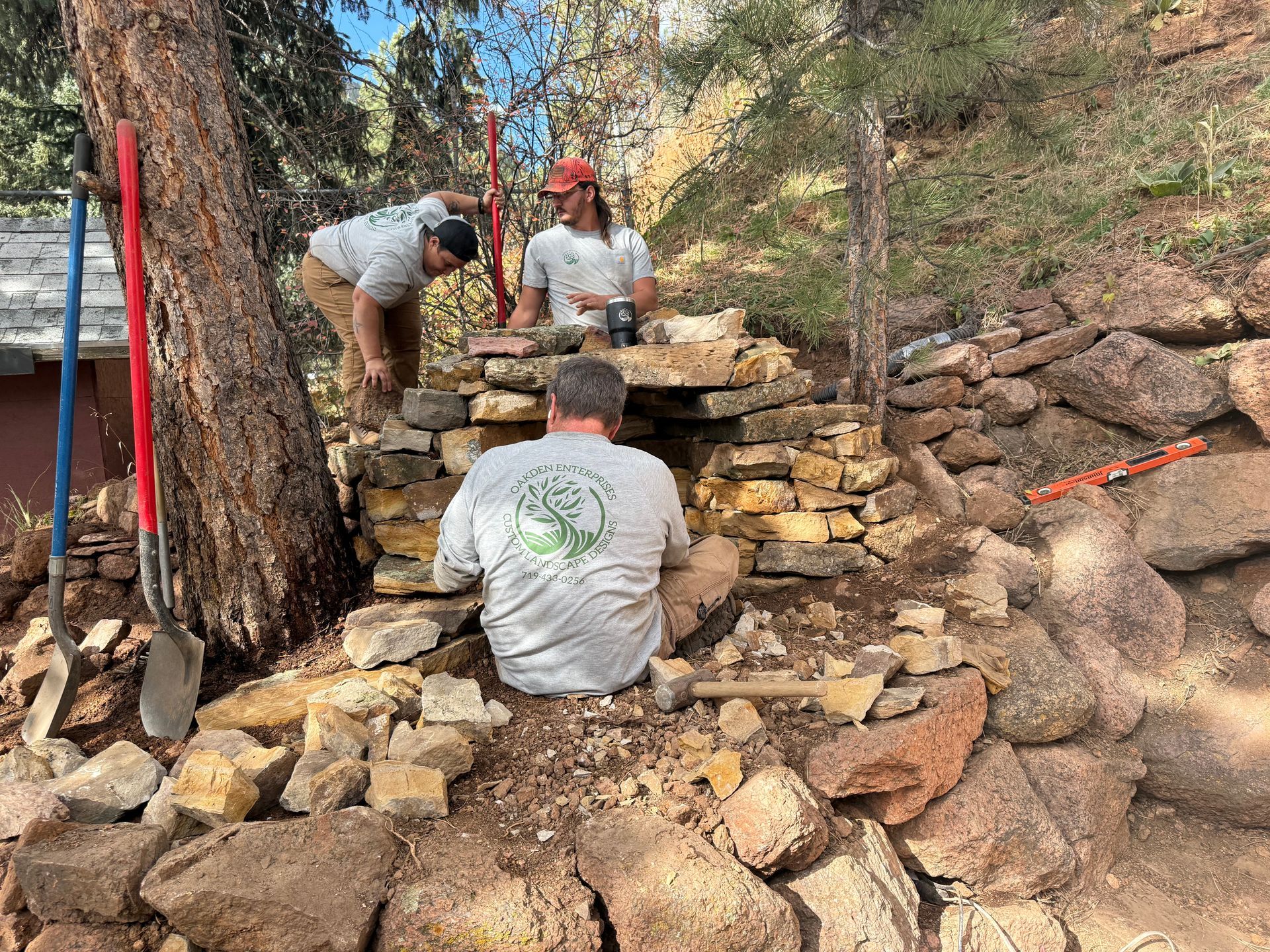 Three workers stacking stones to build a dry stone wall in a wooded outdoor area