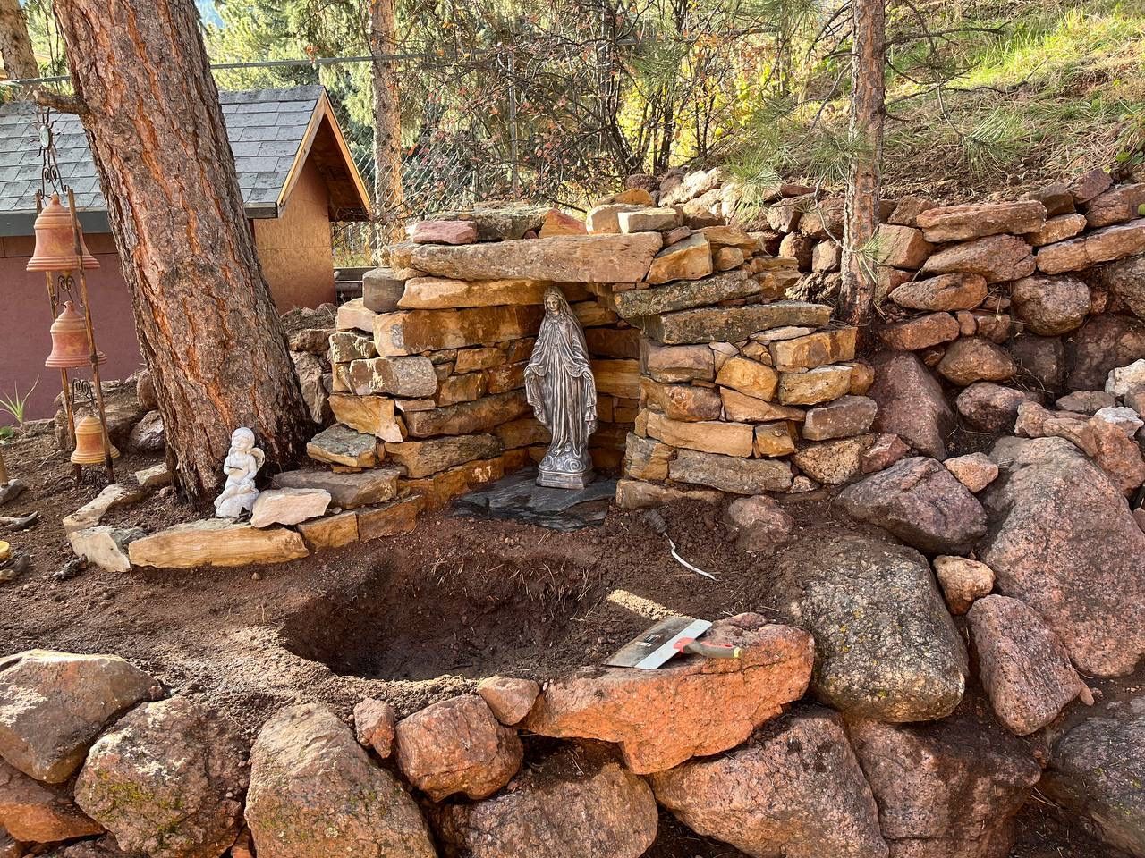 Stone outdoor basin with two small waterfalls in a wooded area, beside a small cabin