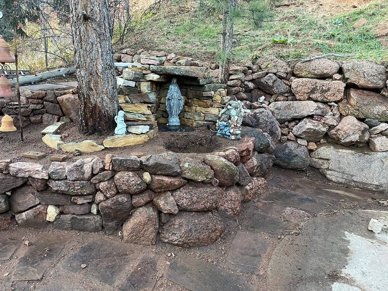 Stone garden altar beneath a tree, with stacked rocks and small blue figurines among autumn leaves