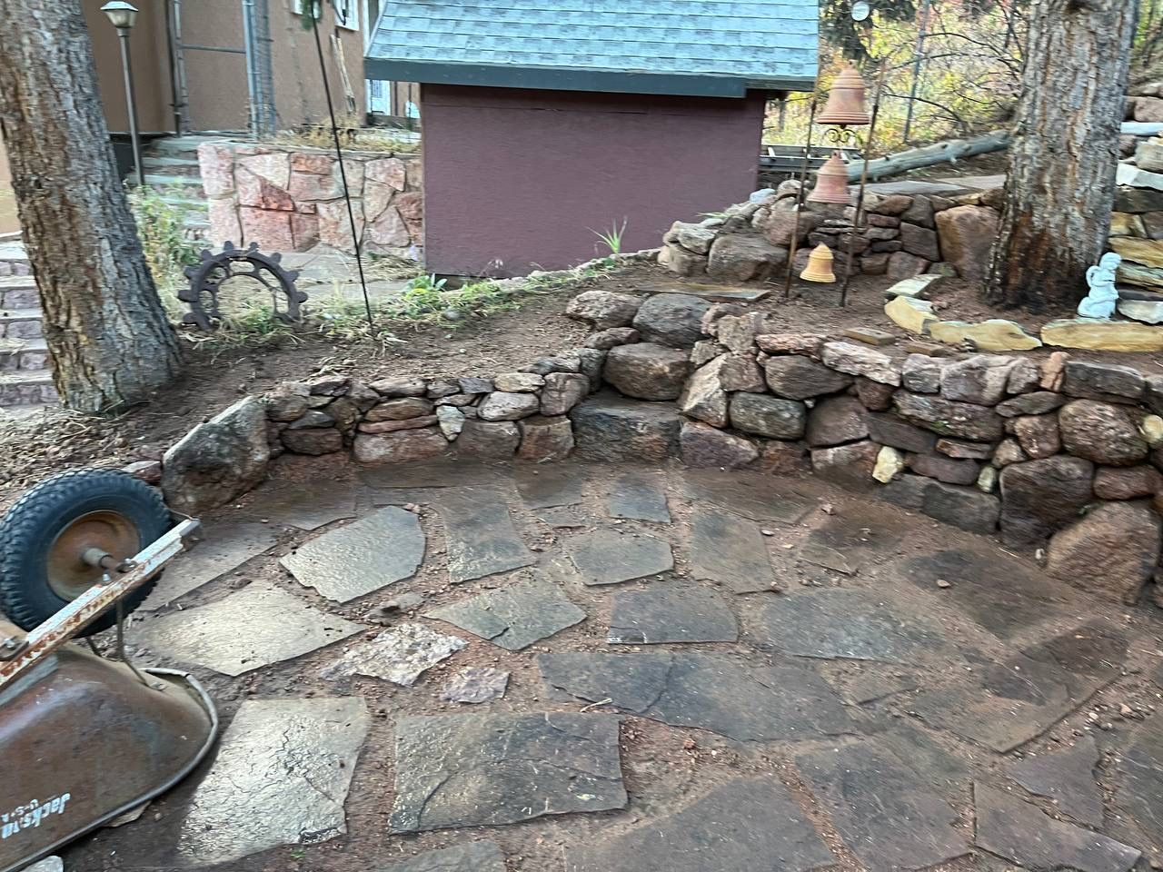 Stone patio with a curved rock retaining wall and trees in a backyard setting