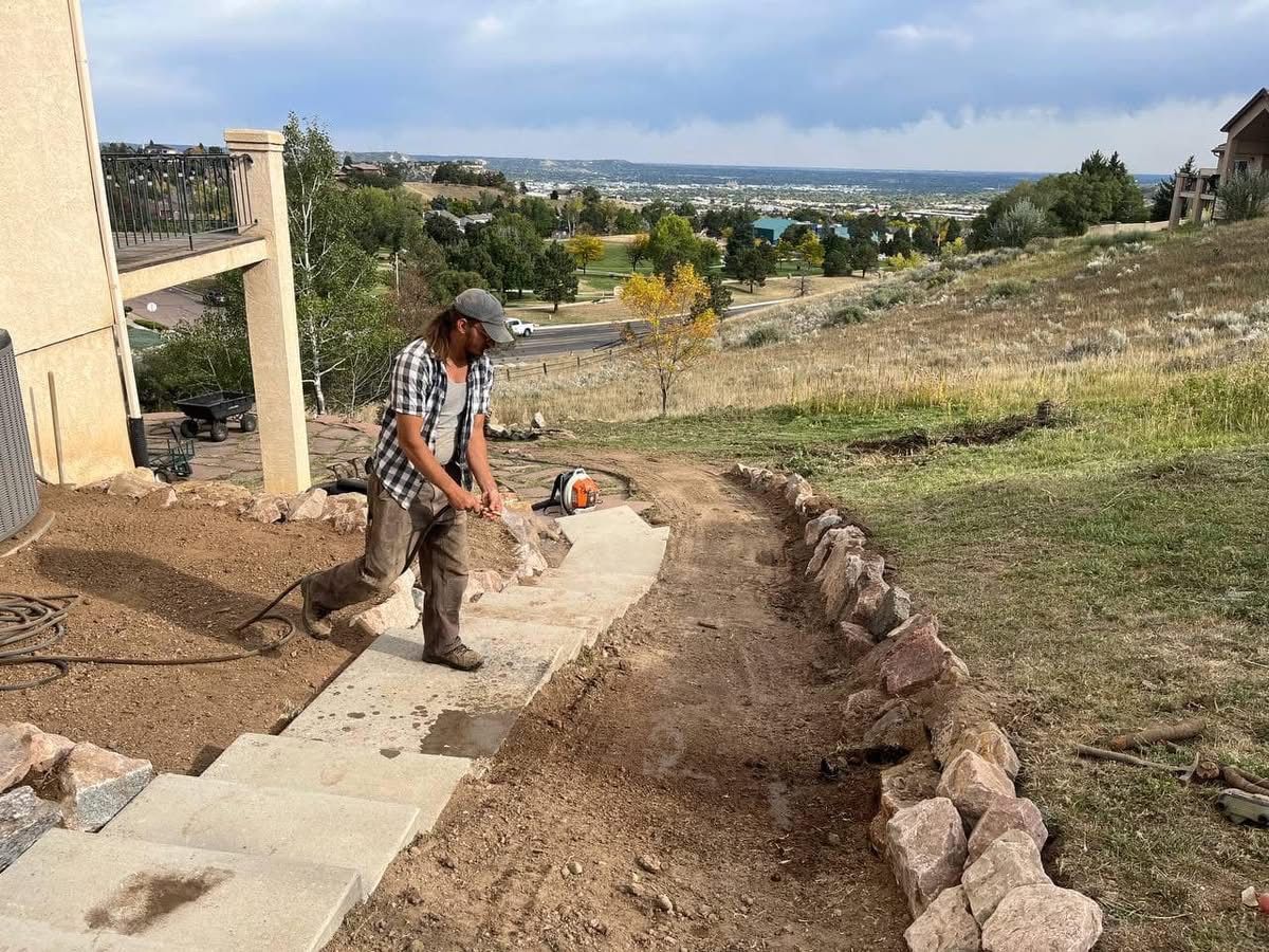 Worker paving a curved path on a hillside with a scenic valley in the background