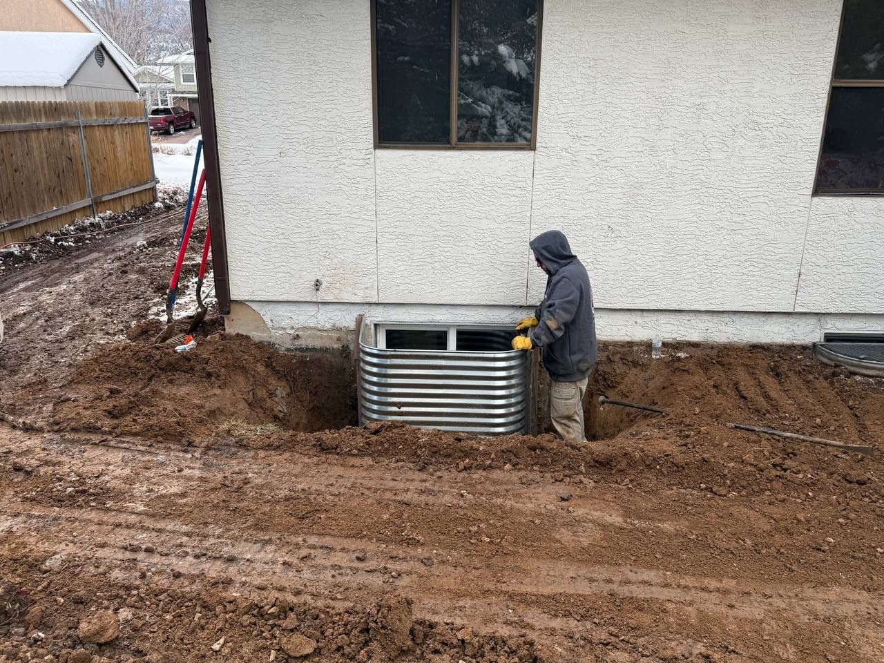 Worker inspecting metal utility box beside house on muddy construction site