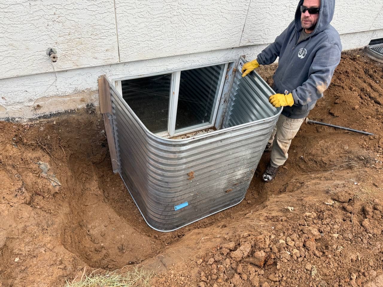 Worker in gloves standing beside a metal utility tank or tank enclosure in a dirt excavation.