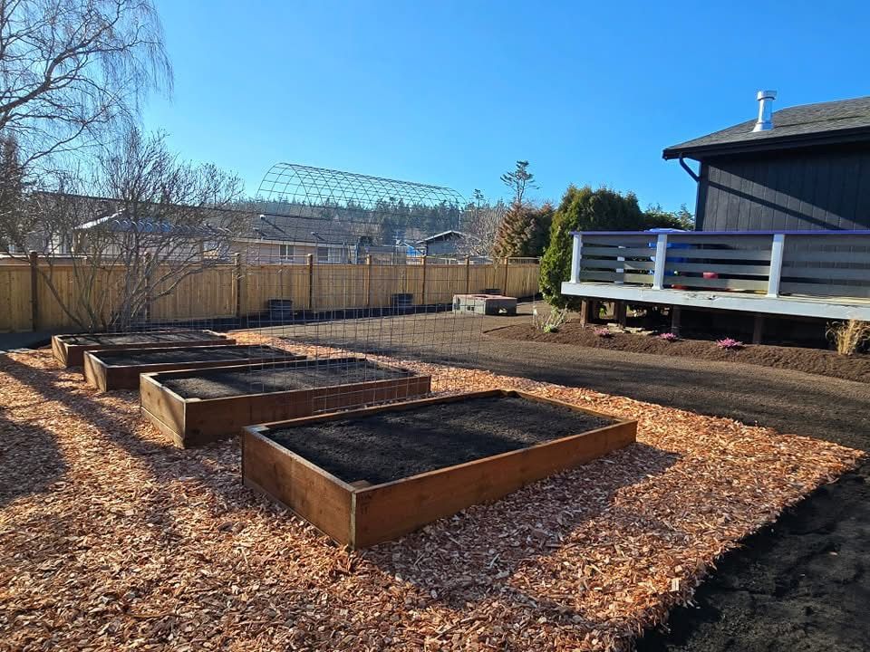 Backyard garden beds with dark soil beside a house and wooden deck on a sunny day