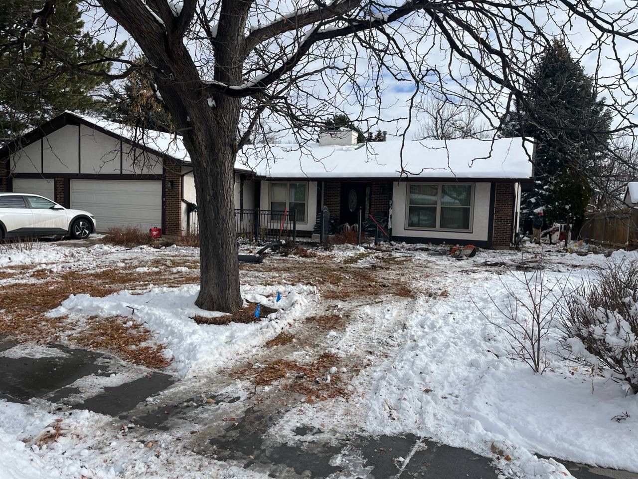 Snow-covered suburban house with bare trees and a car parked in the driveway
