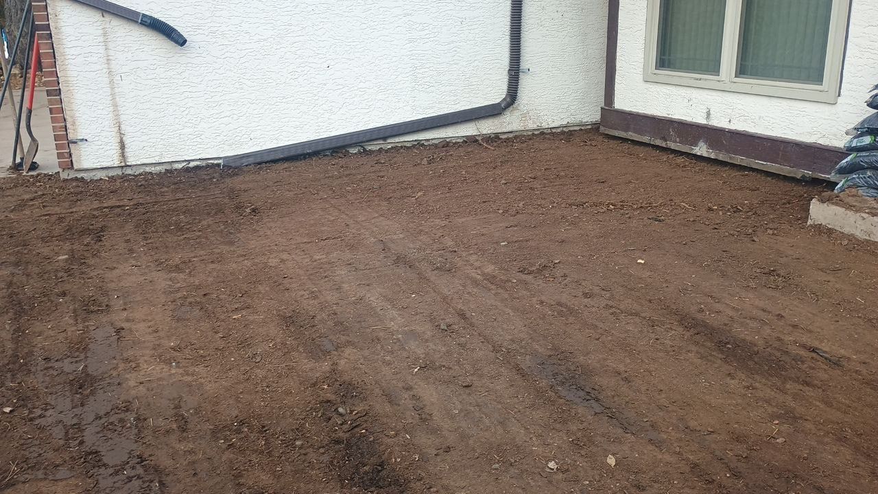 Freshly leveled soil in a backyard beside a white house and sliding glass doors