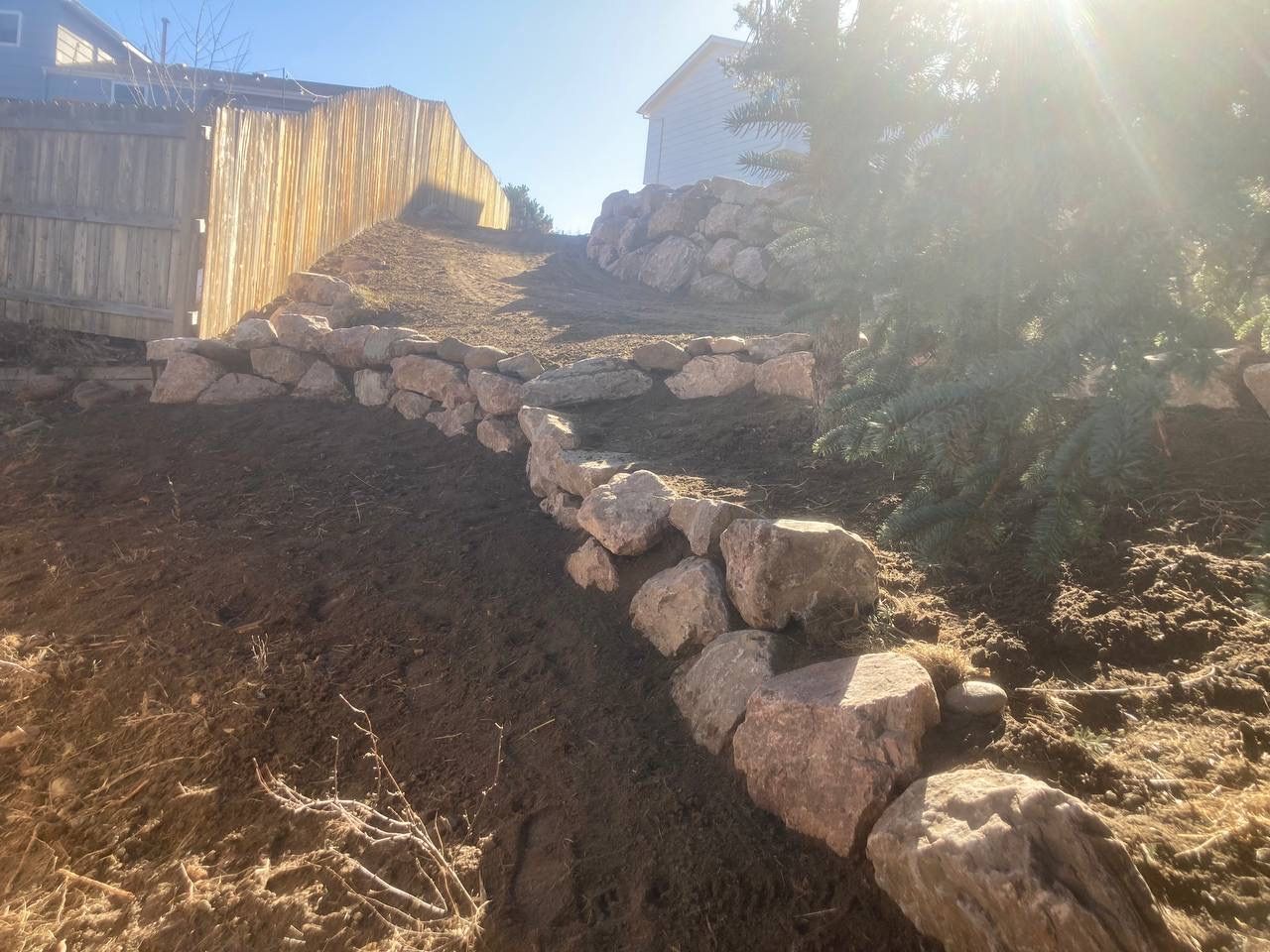 Rock retaining wall on a sloped backyard hillside in bright sunlight