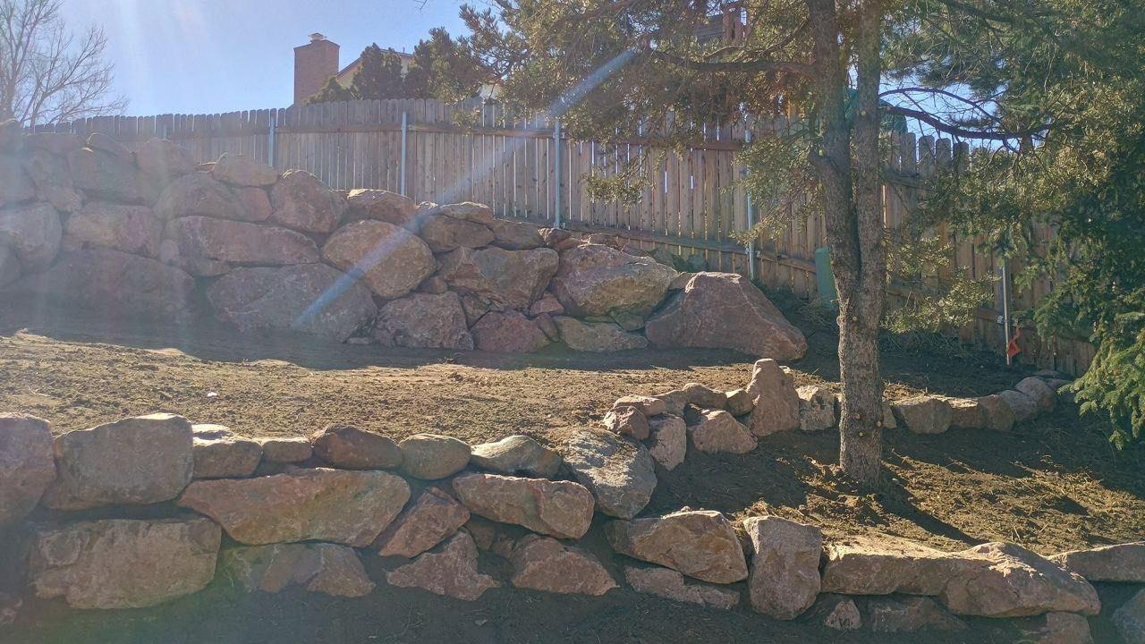 Rock terraced hillside with a tree and sunlit house in the background