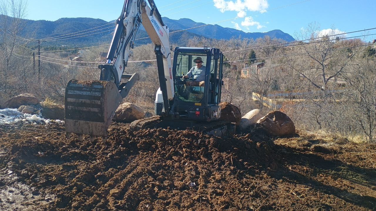 Excavator clearing dirt in a muddy field with mountains in the background