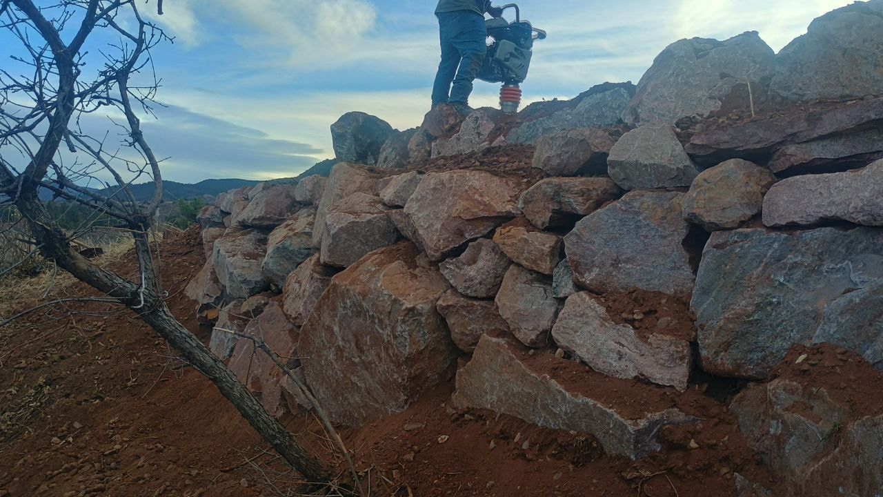 Person standing on a rocky wall outdoors with mountains and cloudy sky in the background