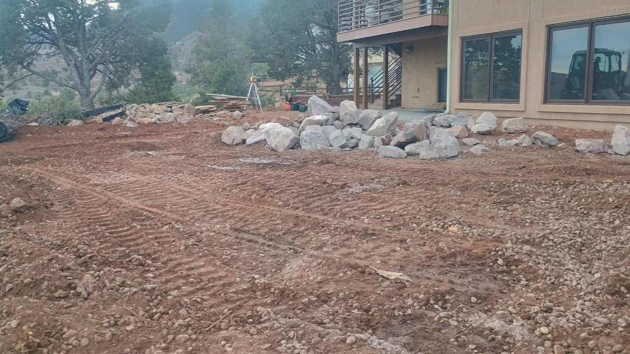 Front yard with freshly graded dirt and a pile of rocks beside a house.
