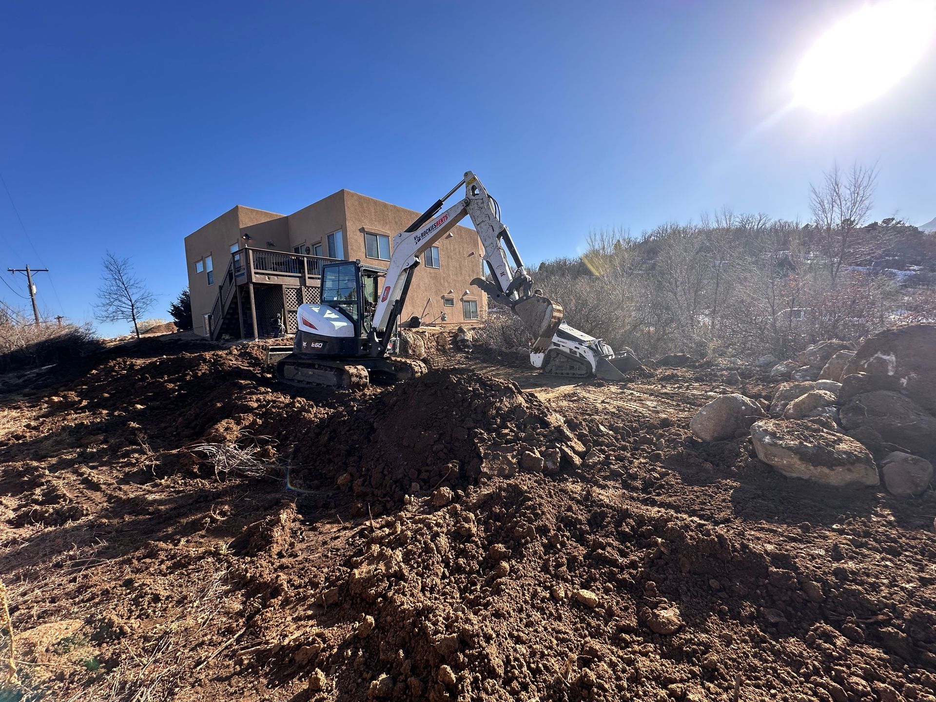 Excavator and dump truck working on a dirt pile at a construction site under a bright blue sky