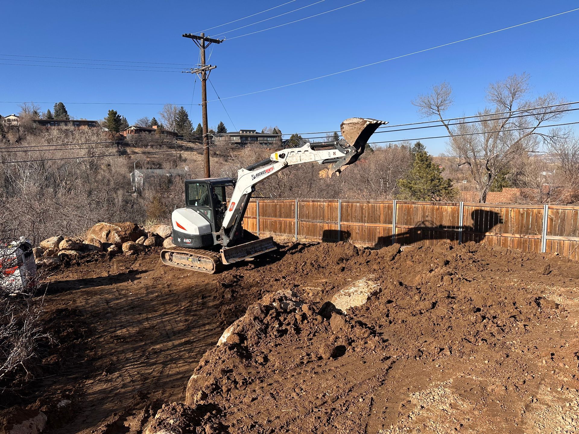 Excavator loading dirt in a fenced construction site under a clear blue sky
