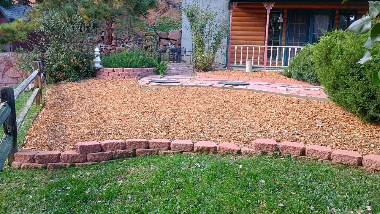Mulched front yard garden bed bordered by red bricks in front of a house porch