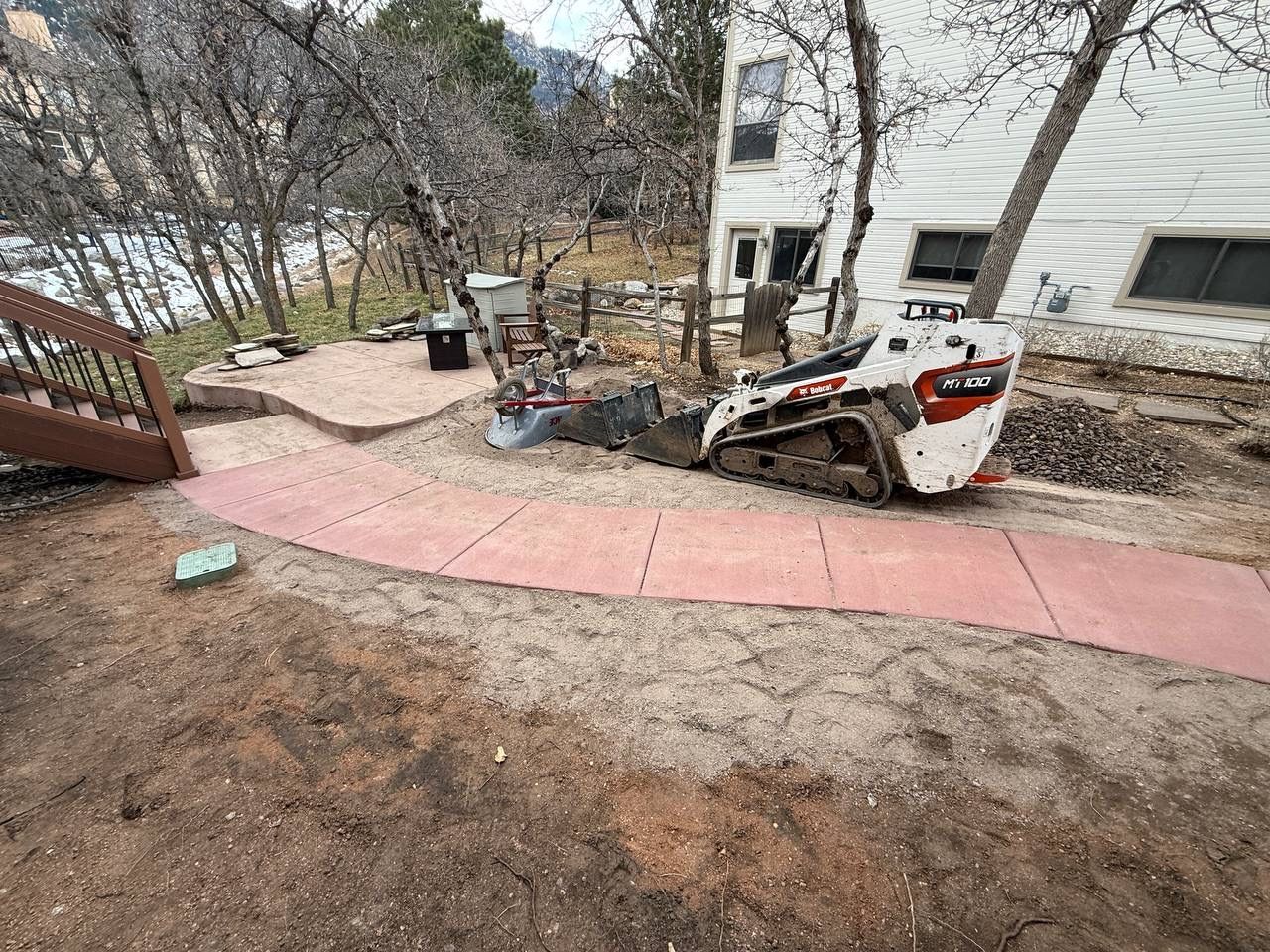 Small construction machine beside a white house and red walkway in a bare backyard